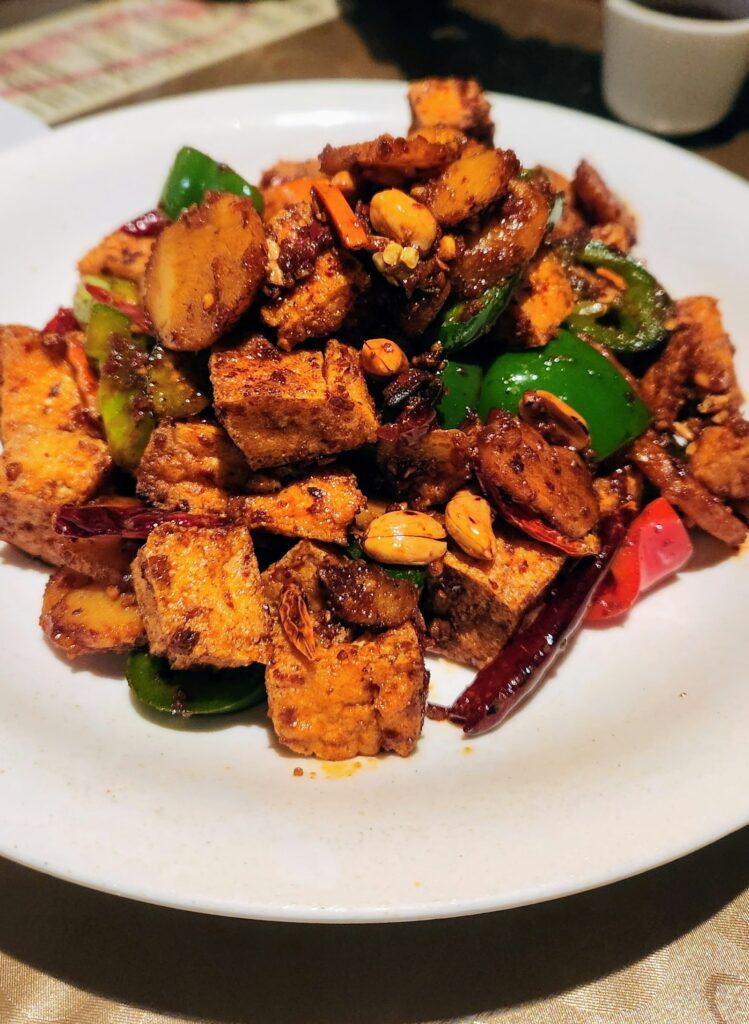 Tofu dourado com pimentões e amendoim servido em prato branco